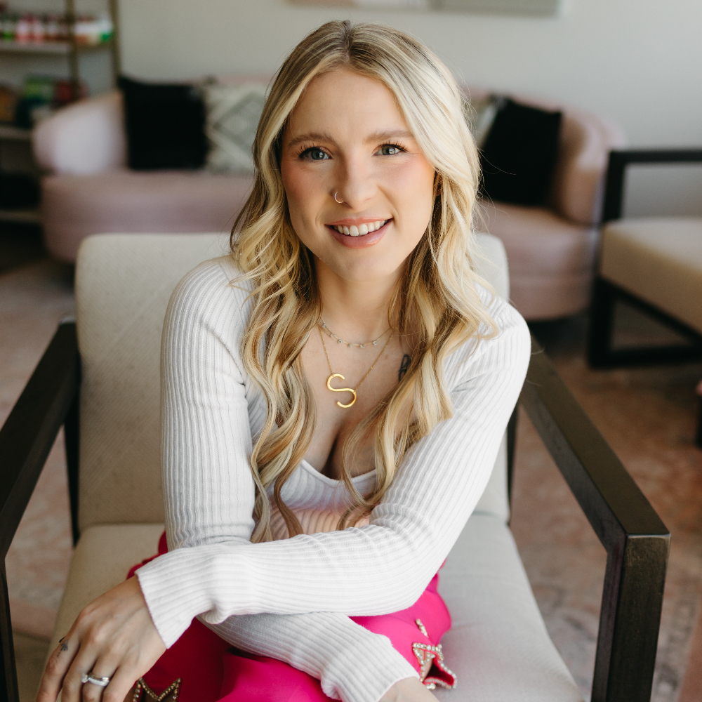 Blonde woman sitting in a chair and smiling at the camera.