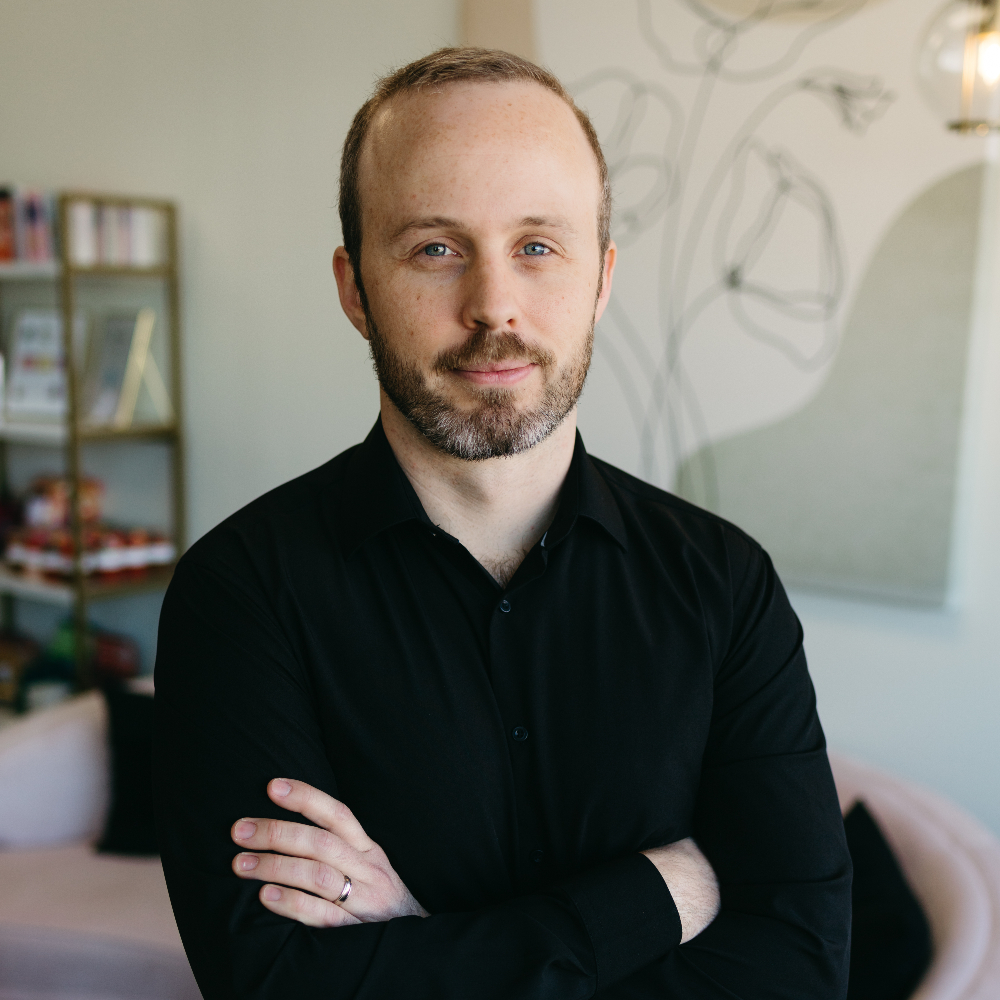 Man with his arms crossed in a black button-down shirt.