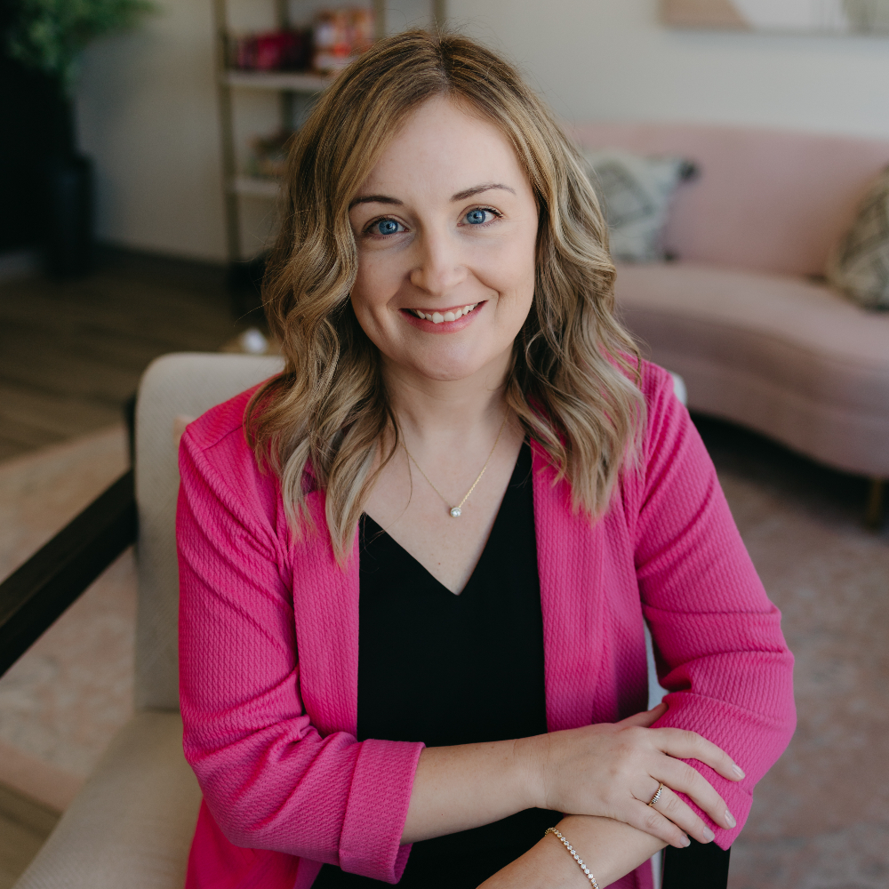 Blonde woman leaning against a counter smiling.